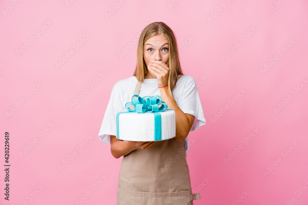 Young russian baker woman holding a delicious cake shocked covering mouth with hands. Young russian baker woman holding a delicious cake shocked covering mouth with hands.