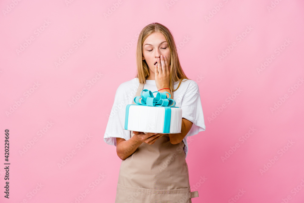 Young russian baker woman holding a delicious cake yawning showing a tired gesture covering mouth with hand. Young russian baker woman holding a delicious cake yawning showing a tired gesture covering mouth with hand.