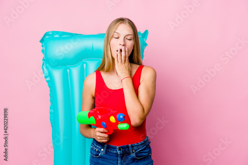 Young russian woman playing with a water gun with an air mattress yawning showing a tired gesture covering mouth with hand.