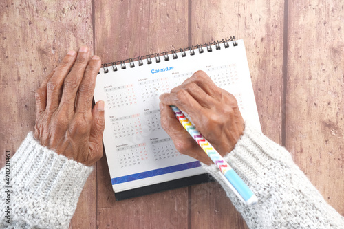 senior women hand with pen circle on date on 2021 calendar on wooden background 