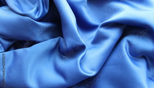 a carelessly crumpled silk fabric in metallic blue for an elegant look. drapery with smooth curves and embossed folds, fabric background in deep blue color, effectively flowing waves of silk 