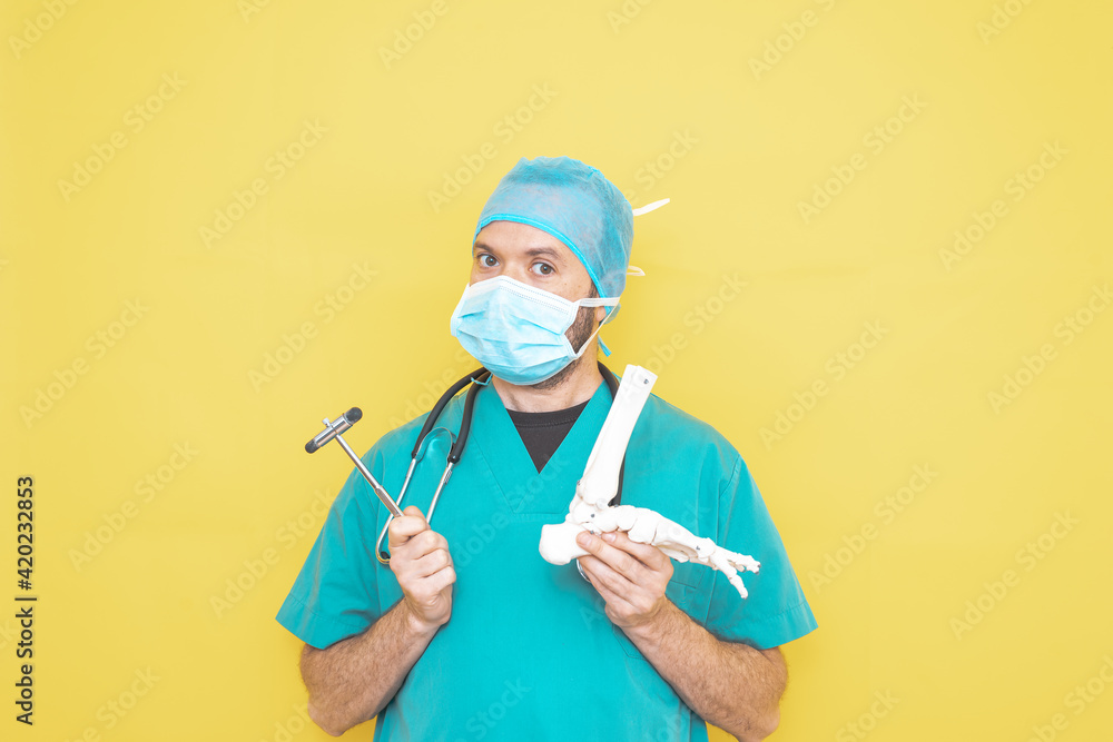Trauma surgeon wearing an operating theatre uniform and stethoscope, checking a skeleton model of a foot, right lower limb, all on a yellow background. Trauma surgeon wearing an operating theatre uniform and stethoscope, checking a skeleton model of a foot, right lower limb, all on a yellow background.