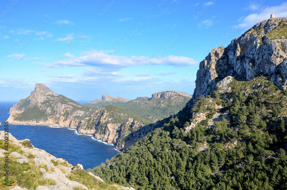 Peninsula Formentor on Balearic island Mallorca, Spain, view from observation platform Creueta or Colomer towards the coastline, watchtower Albercutz on the mountain right, blue sky background