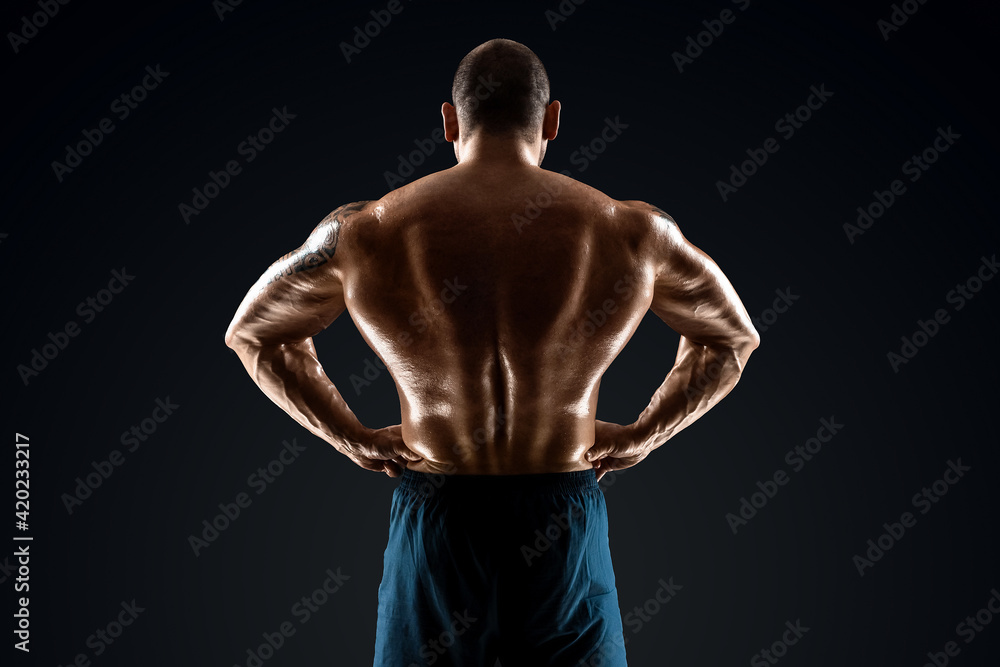 Fototapeta premium Male bodybuilder with light stubble and bare torso shows muscularity against a dark background. The concept of a fitness club, doing sports, weightlifting. Copy space.