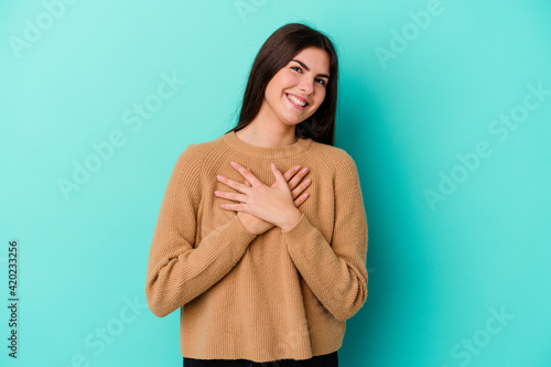 Young caucasian woman isolated on blue background has friendly expression, pressing palm to chest. Love concept.