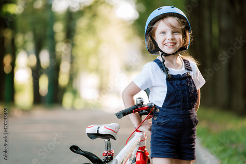 Cheerful smiling girl in blue helmet standing near bicycle.
