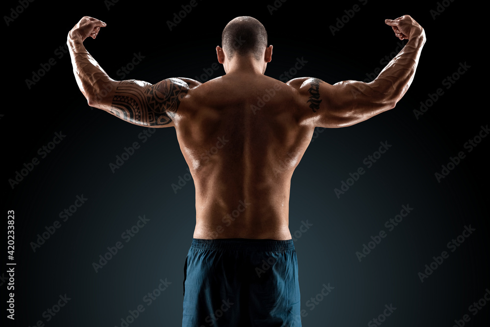 Male bodybuilder with light stubble and bare torso shows muscularity against a dark background. The concept of a fitness club, doing sports, weightlifting. Copy space.