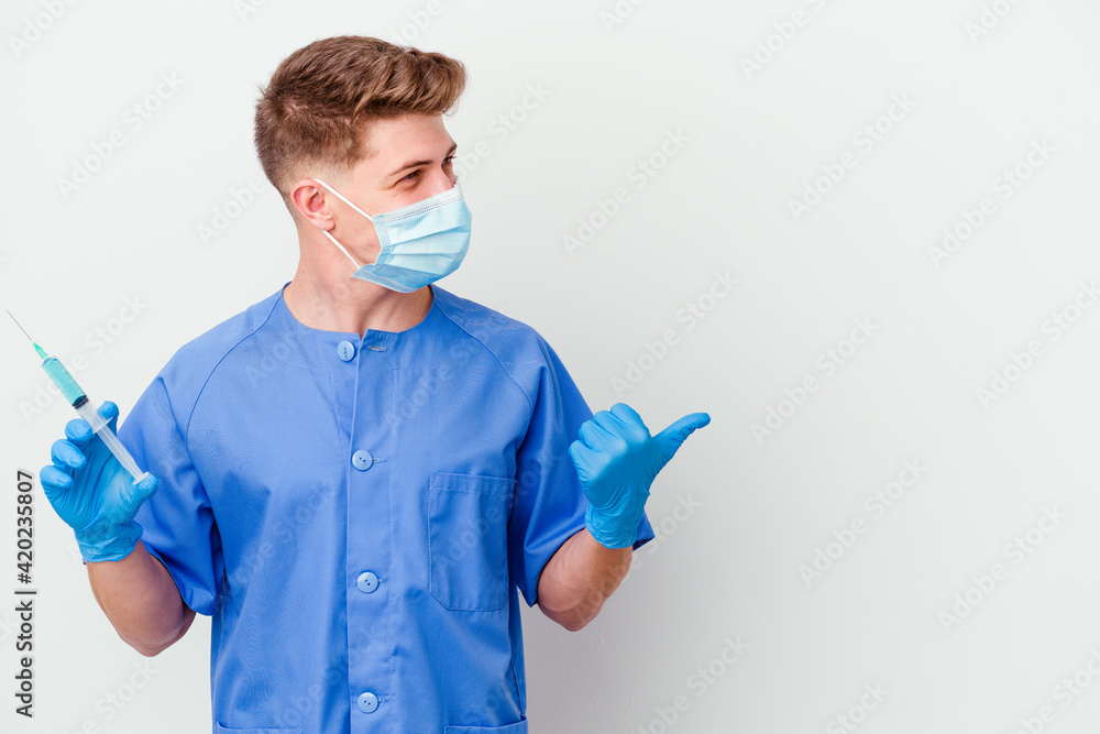 Young caucasian nurse man prepared to give a vaccine isolated on white background points with thumb finger away, laughing and carefree.