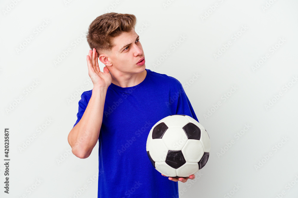 Young caucasian man playing soccer isolated on background trying to listening a gossip. Young caucasian man playing soccer isolated on background trying to listening a gossip.