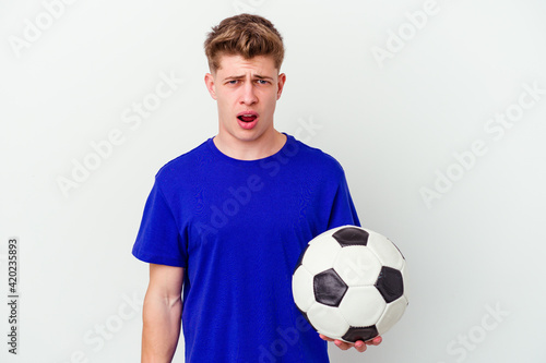 Young caucasian man playing soccer isolated on background screaming very angry and aggressive.