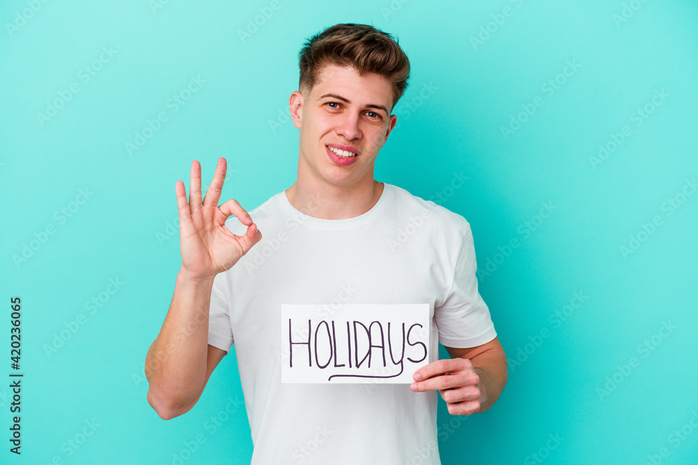 Young caucasian man holding a Holidays placard isolated on blue background Young caucasian man holding a Holidays placard isolated on blue background