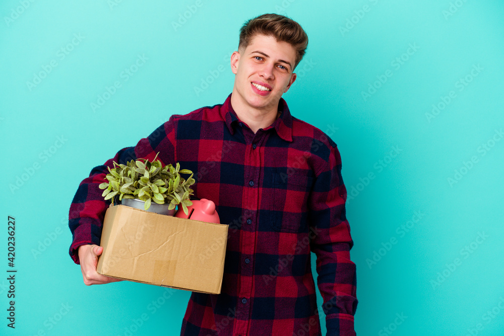 Young caucasian man moving holding a box isolated on blue background happy, smiling and cheerful. Young caucasian man moving holding a box isolated on blue background happy, smiling and cheerful.