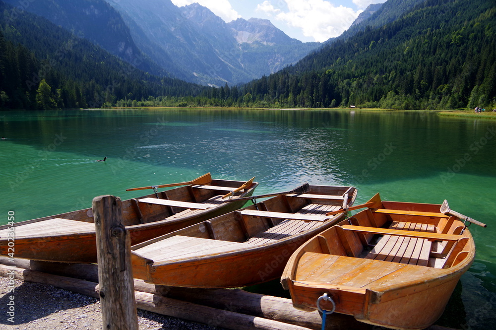Wunderschöner Bergsee mit türkisfarbenen Wasser und 3 Ruderbooten aus Holz am Ufer 