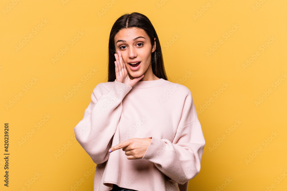Young Indian woman isolated on yellow background saying a gossip, pointing to side reporting something. Young Indian woman isolated on yellow background saying a gossip, pointing to side reporting something.