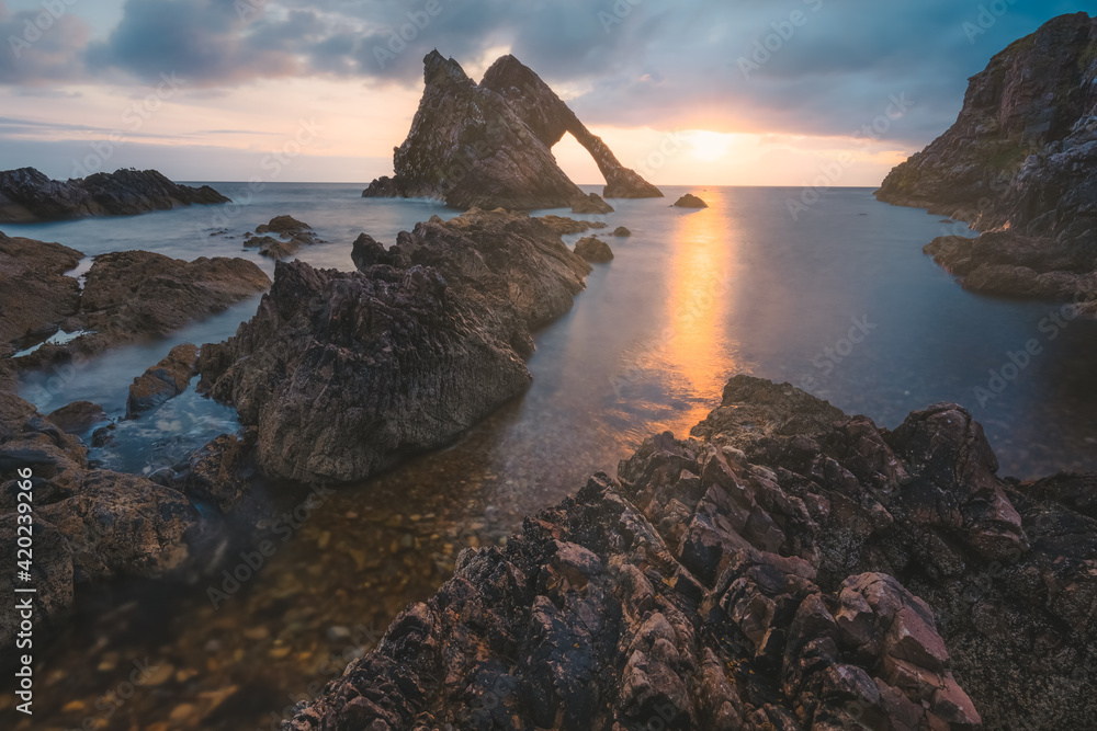 Beautiful dramatic sescape scenery at sunrise or sunset of Bow Fiddle Rock sea arch on the rocky shore of Portknockie on the Moray Firth in Scotland.