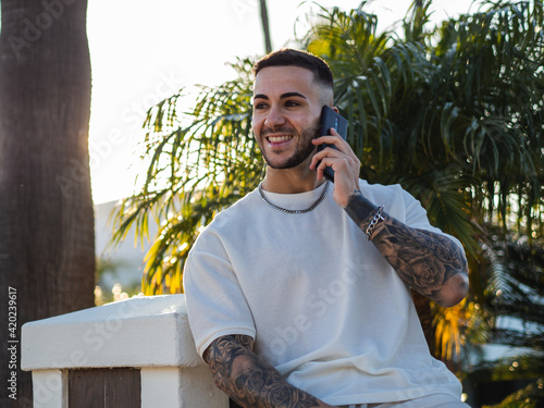 Hombre joven con tatuajes usando su telefono móvil