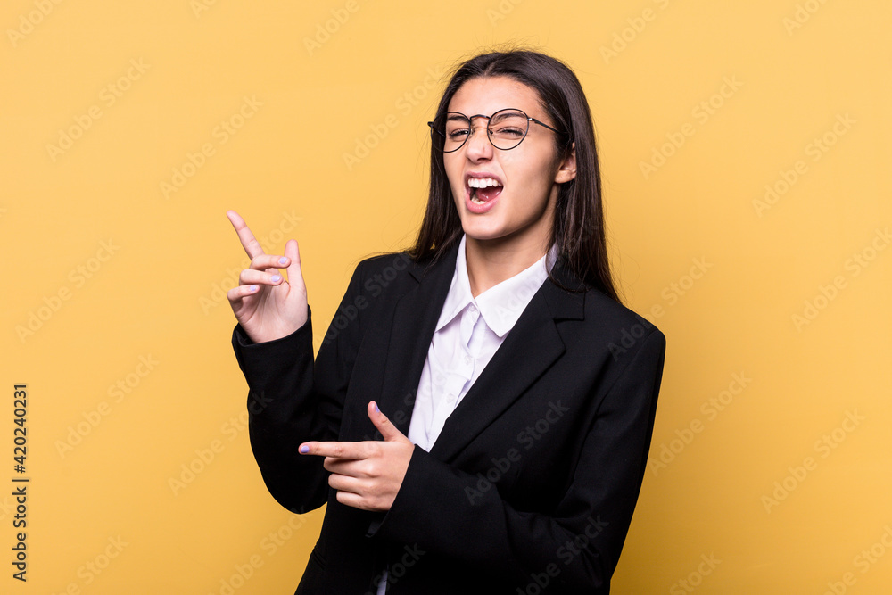 Young Indian business woman isolated on yellow background pointing with forefingers to a copy space, expressing excitement and desire. Young Indian business woman isolated on yellow background pointing with forefingers to a copy space, expressing excitement and desire.