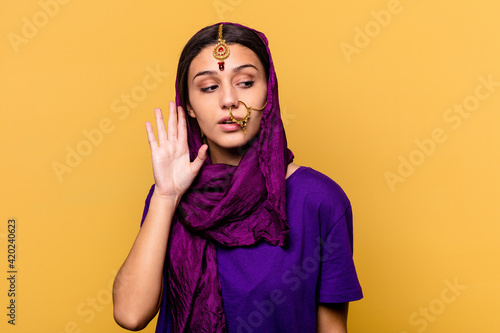Young Indian woman wearing a traditional sari clothes isolated on yellow background trying to listening a gossip. © Asier