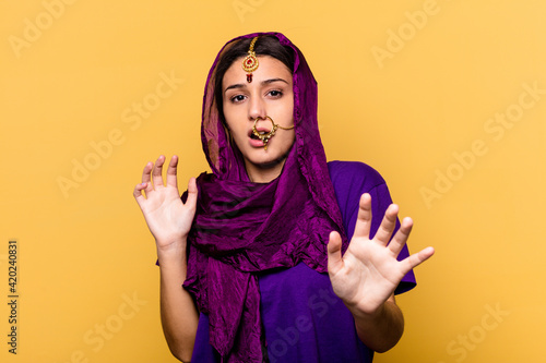 Young Indian woman wearing a traditional sari clothes isolated on yellow background being shocked due to an imminent danger