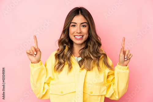 Young caucasian woman isolated indicates with both fore fingers up showing a blank space.