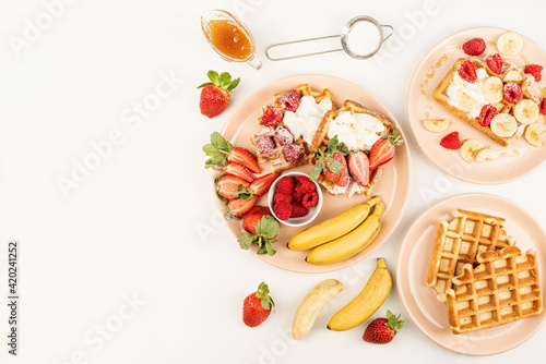 Homemade waffles with fruits and berries, cream and honey in a plate on white table.