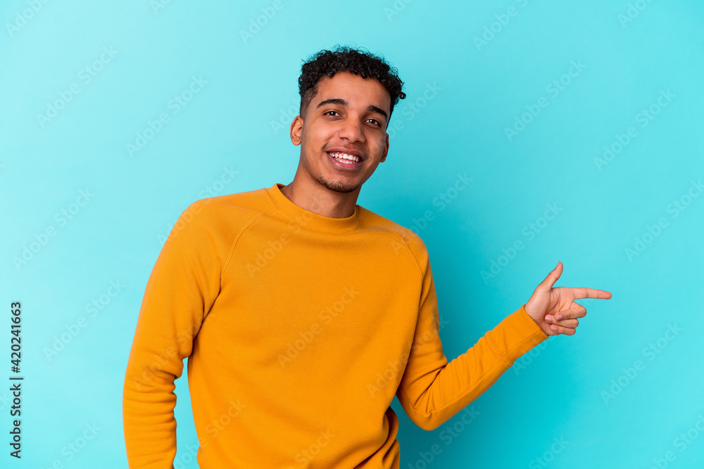 Young african american curly man isolated on blue smiling cheerfully pointing with forefinger away. Young african american curly man isolated on blue smiling cheerfully pointing with forefinger away.