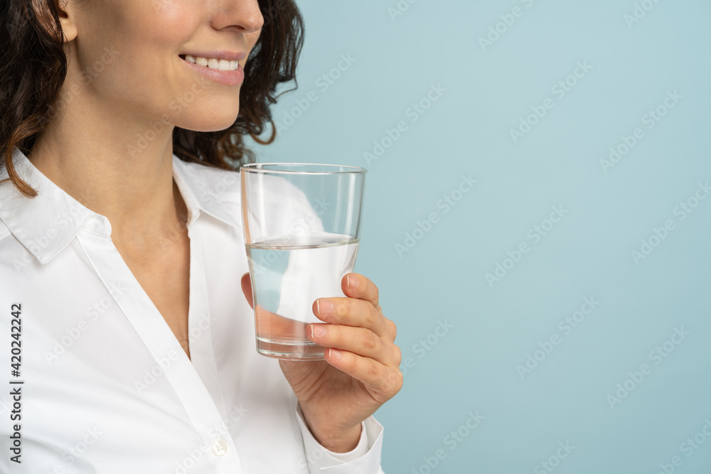 Close up of caucasian woman wear white blouse holding drinking water glass in her hand, isolated on studio blue background. Healthy lifestyle, health care treatment concept. Close up of caucasian woman wear white blouse holding drinking water glass in her hand, isolated on studio blue background. Healthy lifestyle, health care treatment concept.