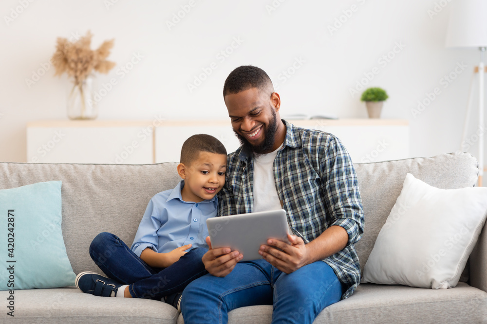 Black Dad And Son Using Digital Tablet Sitting At Home Black Dad And Son Using Digital Tablet Sitting At Home