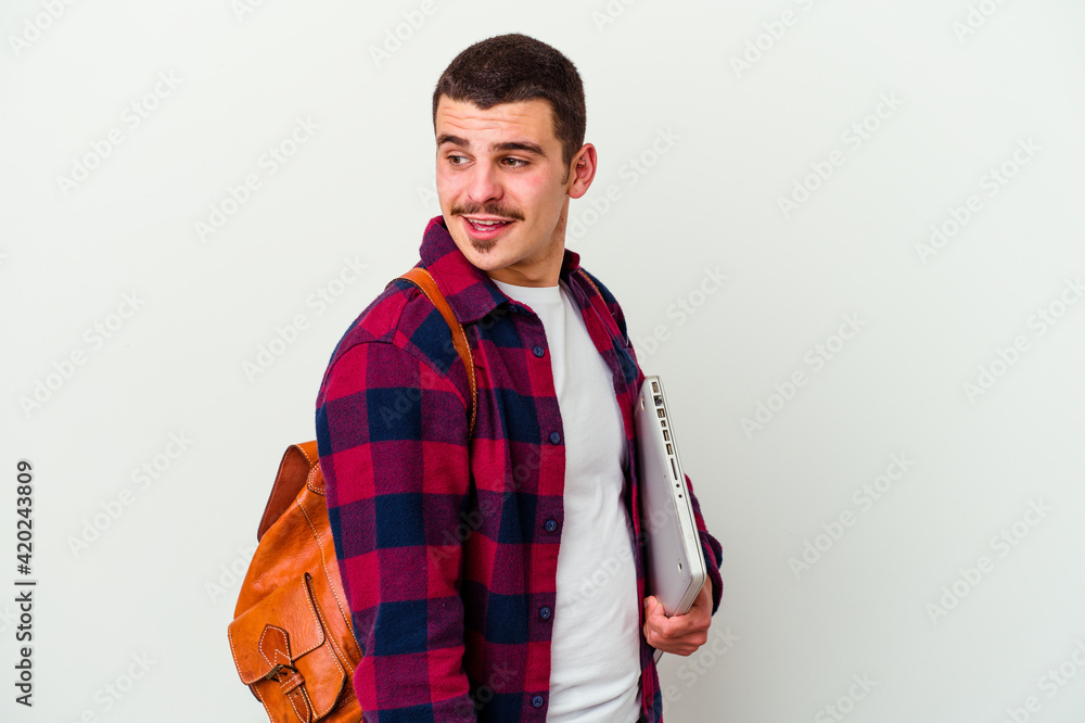Young caucasian student man holding a laptop isolated on white background looks aside smiling, cheerful and pleasant. Young caucasian student man holding a laptop isolated on white background looks aside smiling, cheerful and pleasant.