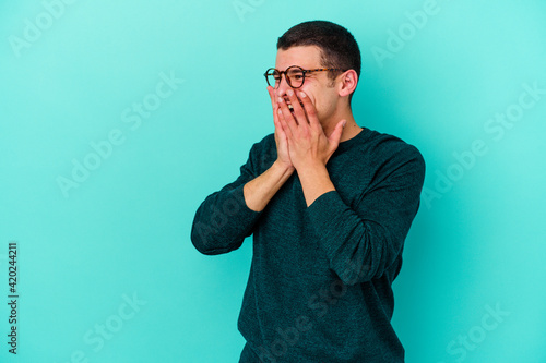 Young caucasian man isolated on blue background laughing about something, covering mouth with hands.