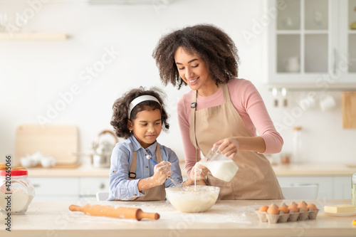 Happy black woman and daughter making pastry in kitchen