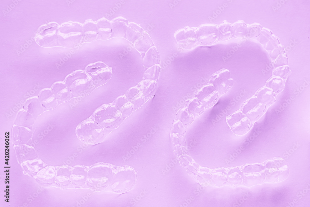 Invisible dental teeth brackets tooth aligners on pink background. Plastic braces dentistry retainers to straighten teeth. Invisible dental teeth brackets tooth aligners on pink background. Plastic braces dentistry retainers to straighten teeth.
