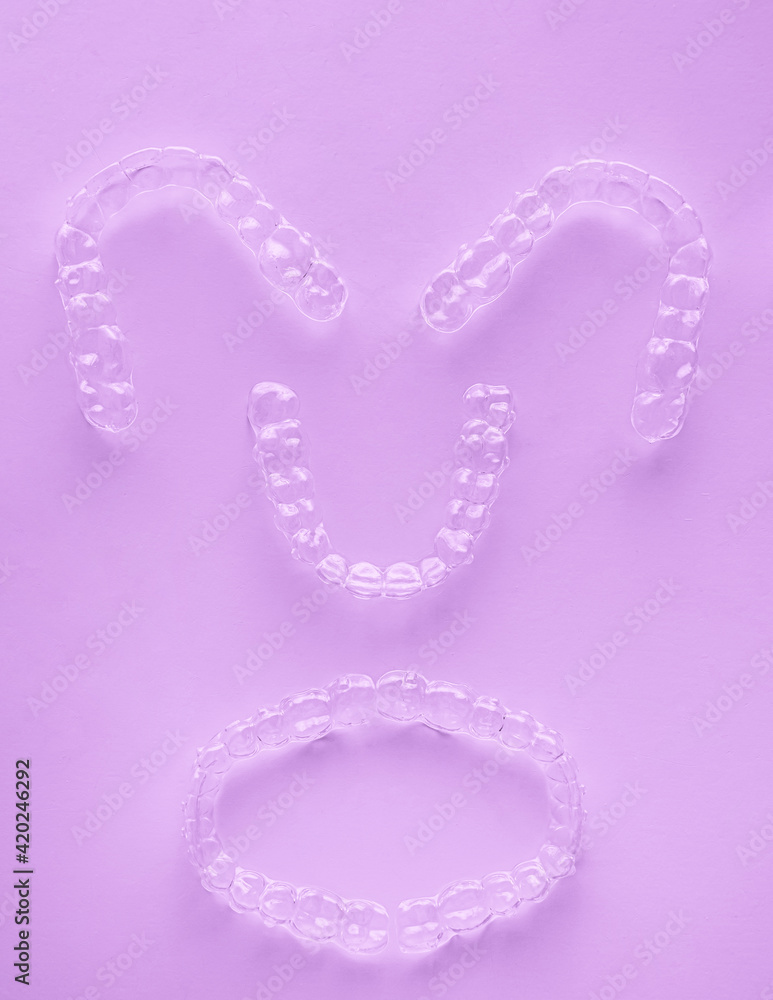 Invisible dental teeth brackets tooth aligners on pink background. Plastic braces dentistry retainers to straighten teeth. Invisible dental teeth brackets tooth aligners on pink background. Plastic braces dentistry retainers to straighten teeth.