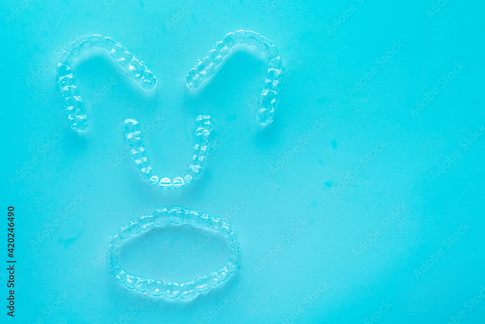 Invisible dental teeth brackets tooth aligners on turquoise background. Plastic braces dentistry retainers to straighten teeth. Invisible dental teeth brackets tooth aligners on turquoise background. Plastic braces dentistry retainers to straighten teeth.