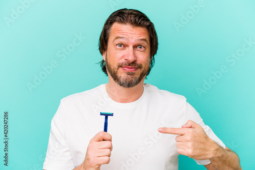Middle age dutch man holding a razor blade isolated on blue background person pointing by hand to a shirt copy space, proud and confident