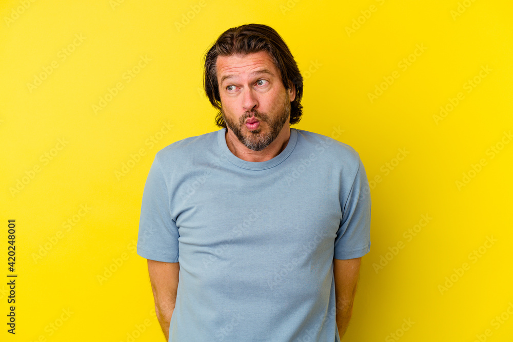 Middle age caucasian man isolated on yellow background shrugs shoulders and open eyes confused. Middle age caucasian man isolated on yellow background shrugs shoulders and open eyes confused.