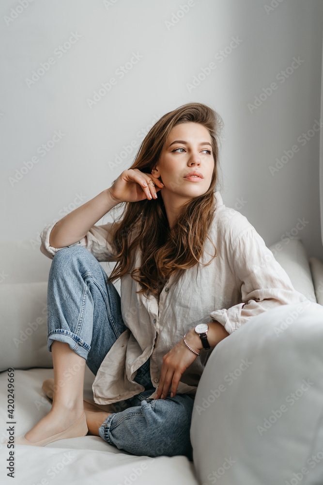 A young blonde woman in casual comfortable clothes sits on a white sofa at home A young blonde woman in casual comfortable clothes sits on a white sofa at home