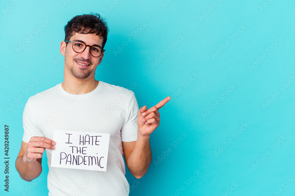 Young caucasian man holding a I hate the pandemic placard isolated smiling and pointing aside, showing something at blank space. Young caucasian man holding a I hate the pandemic placard isolated smiling and pointing aside, showing something at blank space.