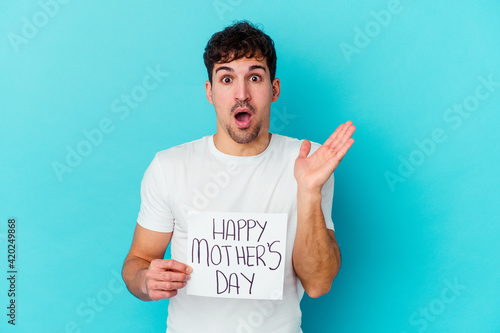 Young caucasian man holding a happy mothers day placard isolated surprised and shocked.