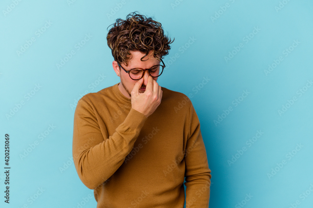 Young caucasian man wearing eyeglasses isolated on blue background having a head ache, touching front of the face. Young caucasian man wearing eyeglasses isolated on blue background having a head ache, touching front of the face.