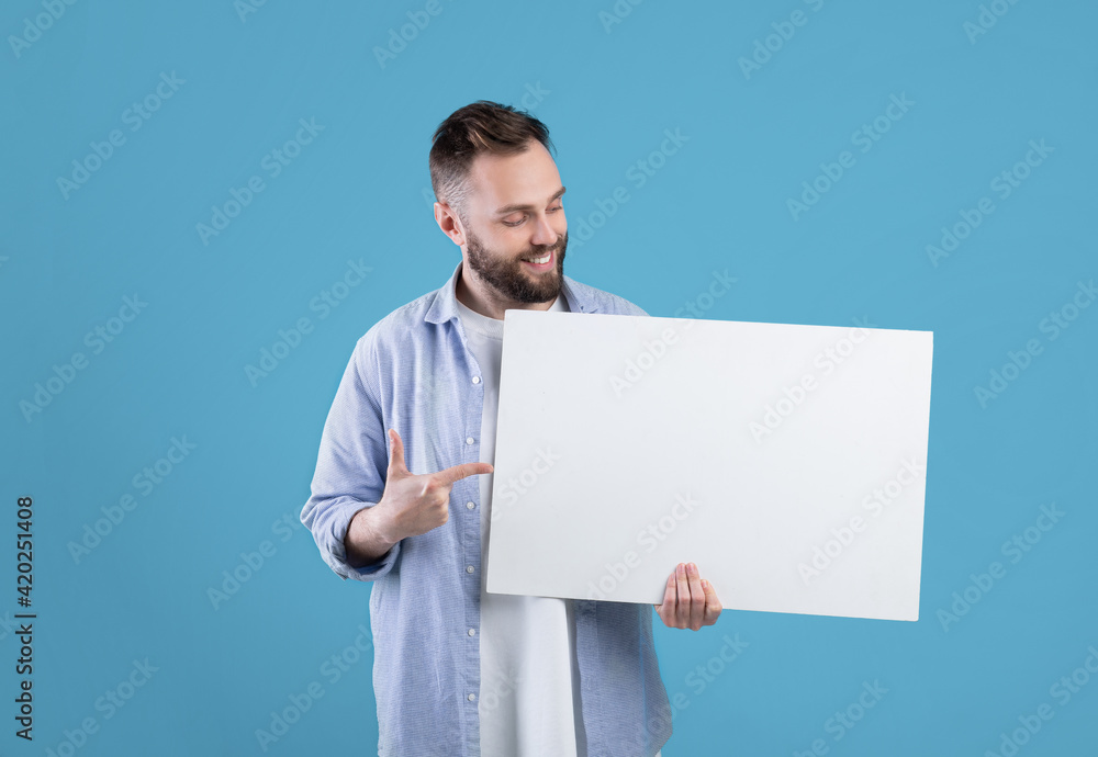 Portrait of positive young guy pointing at blank advertising billboard with mockup for your design Portrait of positive young guy pointing at blank advertising billboard with mockup for your design