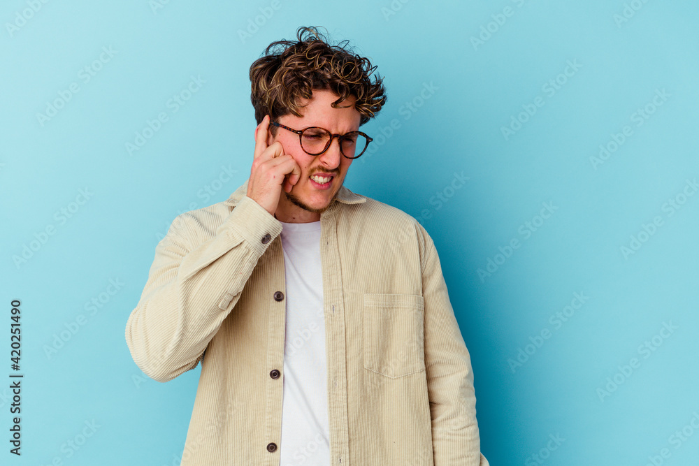 Young caucasian man wearing eyeglasses isolated on blue background covering ears with hands. - obrazy, fototapety, plakaty 