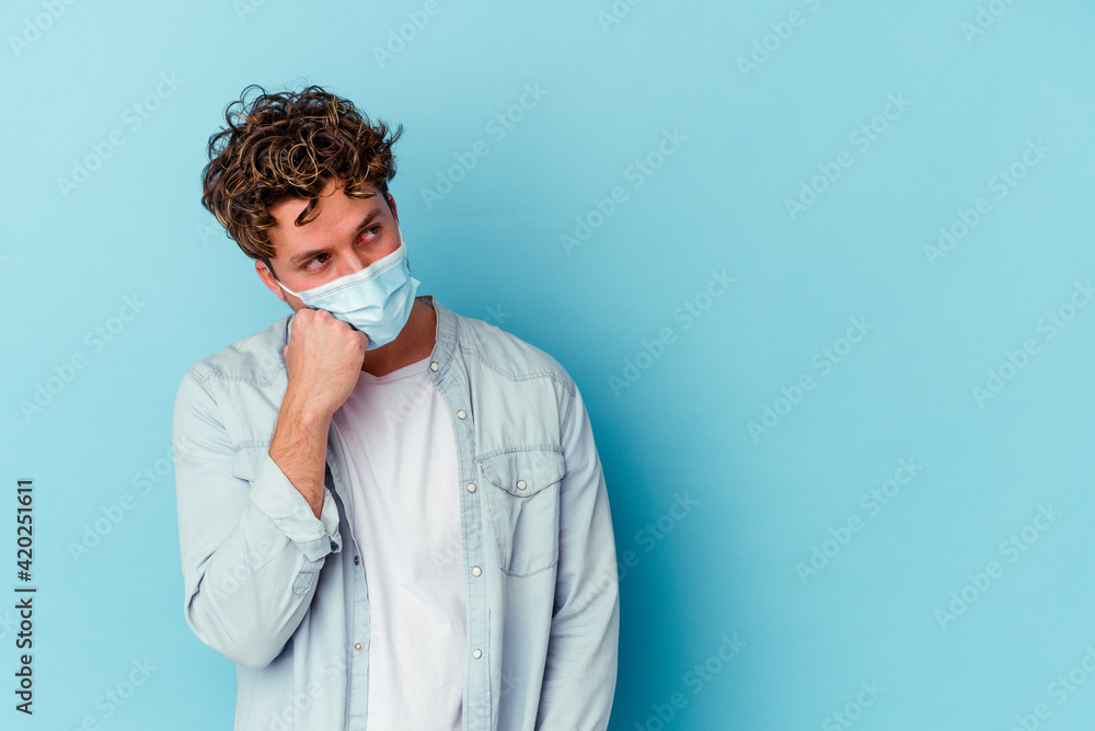 Young caucasian man wearing an antiviral mask isolated on blue background who feels sad and pensive, looking at copy space. Young caucasian man wearing an antiviral mask isolated on blue background who feels sad and pensive, looking at copy space.
