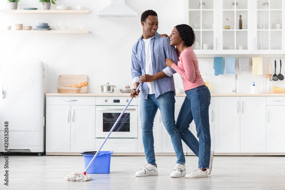 Beautiful african american couple mopping floor in kitchen Beautiful african american couple mopping floor in kitchen