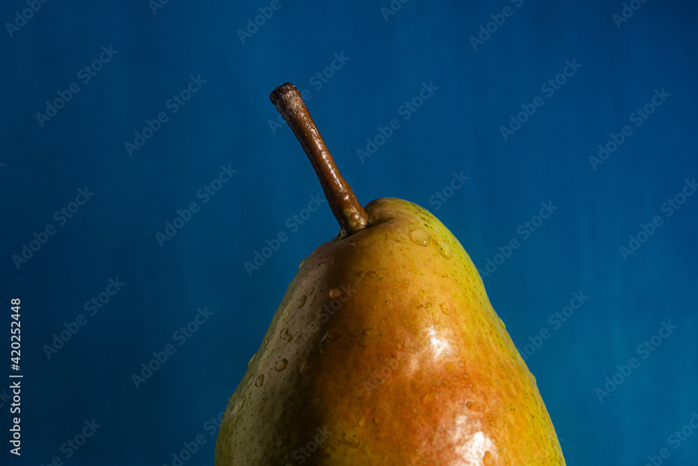 ripe pear with water drops in front of blue, as a close-up