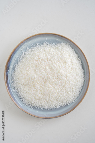 Bird's eye view of a plate with desiccated coconut, raw dried coconut shaving, white background, with copy space