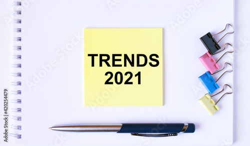 Yellow sticker with text Trends 2021 lying on a white Notepad with a pen and paper clips