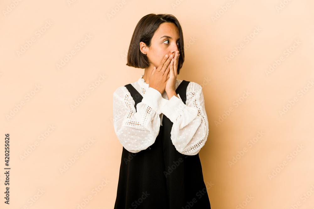 Young hispanic woman isolated thoughtful looking to a copy space covering mouth with hand. Young hispanic woman isolated thoughtful looking to a copy space covering mouth with hand.