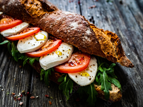 Obraz na plátně Caprese sandwich with tomato, mozzarella and arugula on wooden table