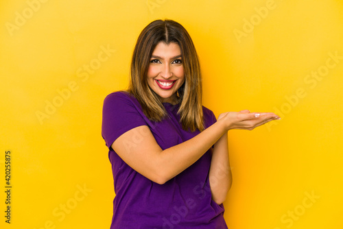 Young indian woman isolated on yellow background holding a copy space on a palm. © Asier